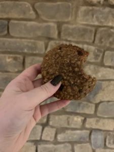 a lactation cookie held in the air in front of a rustic brick wall